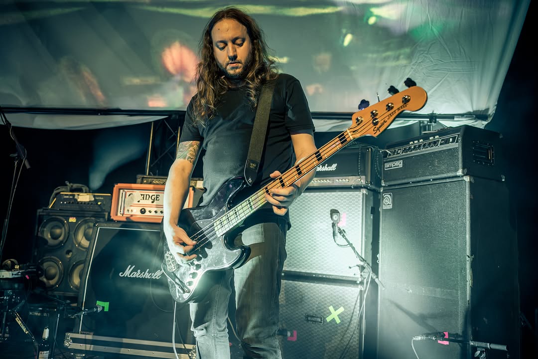 Forkalyst live: bassist Daniel playing the bass guitar with a focused expression in front of a variety of amplifiers.
